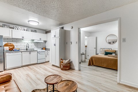 Fusion Fort Worth Apartments renovated kitchen area in Haltom City, TX with light wood plank flooring and subway tile backsplash, white appliances, and large bedroom door.